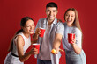 © Pixel-Shot - Young friends with cups and ball for beer pong on red background