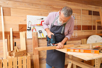 Sticker - Mature carpenter sawing wooden board with jigsaw at table in workshop