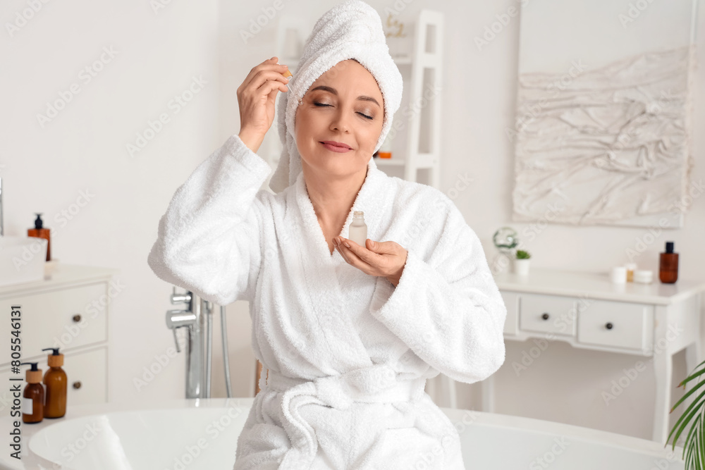 Mature woman applying serum after shower in bathroom