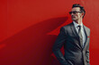 © Nomi - A vision of sophistication, a suave gentleman stands tall agnst a solid red background, his immaculate business attire accentuating his natural allure.