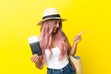 Wall Mural - Young mixed race woman holding passport and beach bag isolated on yellow background pointing finger to the side and presenting a product