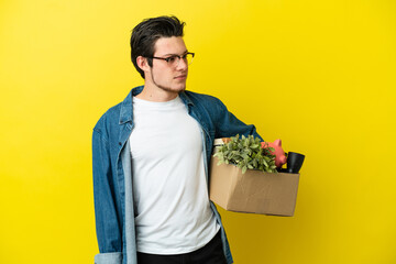 Wall Mural - Russian Man making a move while picking up a box full of things isolated on yellow background looking to the side