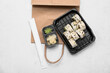 Plastic plate with tasty sushi rolls, chopsticks and paper bag on white grunge background. Delivery concept
