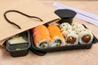 Plastic plate with tasty sushi rolls, marinated ginger and paper bag on beige grunge background, closeup. Delivery concept