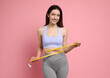 Happy young woman with measuring tape showing her slim body on pink background