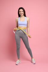 Canvas Print - Happy young woman with measuring tape showing her slim body on pink background