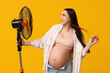 Pregnant young woman with electric fan on yellow background