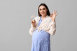 Pregnant young woman with small electric fan showing OK gesture on white background