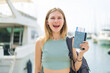 © luismolinero - Young blonde woman holding a passport at outdoors with surprise and shocked facial expression