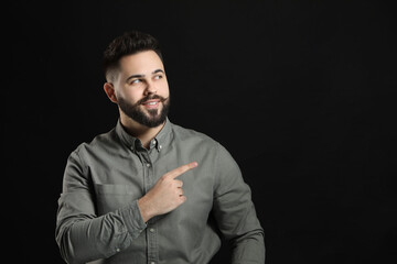 Poster - Young man with mustache pointing at something on black background. Space for text