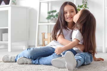 Sticker - Cute little Asian happy sisters kissing on floor at home