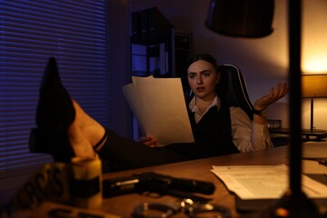 Professional detective working with documents at table in office at night