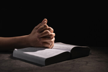 Wall Mural - Religion. Christian woman praying over Bible at table against black background, closeup. Space for text