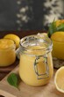 Delicious lemon curd in glass jar, fresh citrus fruits and green leaves on table
