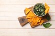Tasty spinach dip with eggs in bowl and nachos chips on light wooden table, top view. Space for text