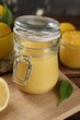 Delicious lemon curd in glass jar, fresh citrus fruit and green leaf on table