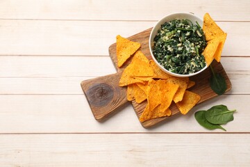 Wall Mural - Tasty spinach dip with eggs in bowl and nachos chips on light wooden table, top view. Space for text