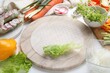 Rice paper and other ingredients for spring rolls on white wooden table