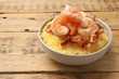 Fresh tasty shrimps, bacon and grits in bowl on wooden table, closeup. Space for text