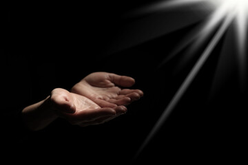 Wall Mural - Christian woman stretching hands towards holy light in darkness, closeup. Prayer and belief