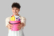 Young man with bucket of cleaning supplies on light background