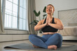 Yoga mindfulness meditation. Woman practicing yoga in living room at home. Plus size female sitting in lotus pose meditating smiling relaxing indoor. Girl doing breathing practice. Yoga at home