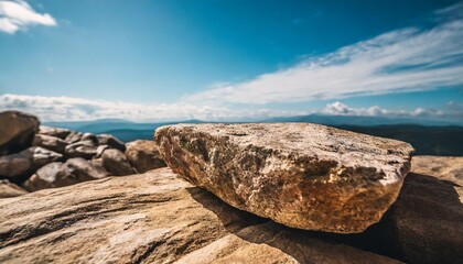 Wall Mural - a horizontal low perspective rock for a product display showing close detail to the rear edge of the stone surface with a blurred cloud and boulder background