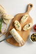 Tasty butter with green onion, olives, garlic and bread on white wooden table, top view