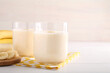 Tasty yogurt in glasses and bananas on white wooden table, closeup. Space for text