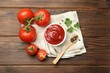 Delicious ketchup in bowl, tomatoes, parsley and peppercorns on wooden table, top view