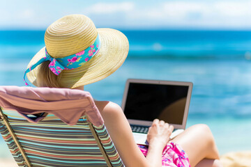 Young woman in straw hat with laptop on the beach. Summer vacation