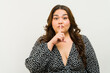 © AntonioDiaz - Curvy woman posing confidently, making a silence gesture with finger on lips in a studio