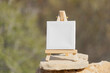 Mockup. White mini canvas on small wooden easel stand standing outdoors with blurred nature background