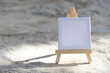 Mockup. White mini canvas on small wooden easel stand standing outdoors on rock stone background