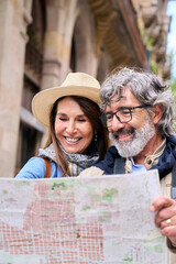 Vertical. Mature couple in sixties smiling looking at map in European city street. Happy seniors enjoying vacation or weekend getaway together. Concept of travel, leisure and lifestyle in retirement