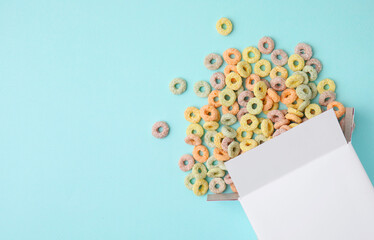 Canvas Print - Paper box with tasty cereal rings on light blue background, flat lay. Space for text