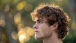 Young man with curly hair looking thoughtfully into the distance.