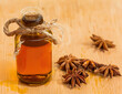 Maceration, spices in a glass on a wooden table. Macerated oil ingredient in a clear sealed bottle with a cork stopper, with star anise. Background with space.