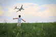 © New Africa - Boy in green field looking at airplane flying in sky, back view
