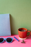 Fototapeta Londyn - Desktop workspace. notebook, eyeglasses, colored pencil, clip, cup of hot chocolate on pink desk. khaki green wall background