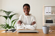 Happy young Black female entrepreneur at home office. African American woman looking at camera sitting at desk.