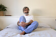 Mature man wearing pyjamas relaxing sitting on the bed looking a camera.