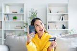 Fototapeta  - Young asian woman lying on sofa in living room, makes online banking payments through the internet from bank card on cell phone. Shopping online on mobile with credit card