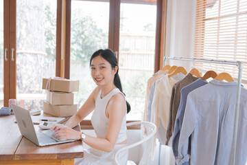 Wall Mural - Beautiful Asian female fashion designers or dressmakers show the sample clothes to the client in the online meeting. Fashion designer working in the studio. Small business concept