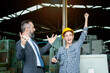 © Stella - Beautiful woman industrial engineer worker wears safety helmet raising hands to celebrate success with businessman boss at manufacturing plant industry factory. People working at workplace.