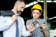 © Stella - Beautiful industrial engineer woman worker wears safety helmet, holds walkie talkie, looks at mobile phone of businessman boss to get information at manufacturing plant industry factory workplace.