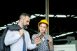 © Stella - Beautiful industrial engineer woman worker wears safety helmet, holds walkie talkie, looks at mobile phone of businessman boss to get information at manufacturing plant industry factory workplace.