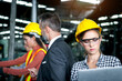 © Stella - Young beautiful woman industrial engineer worker with helmet and safety glasses using laptop computer for operating machinery at manufacturing plant factory with coworkers as blurred background.