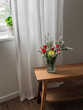 A bouquet of tulips and spiraea on a wooden bench near the window in the living room