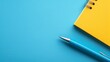   A blue and yellow notebook sits atop a pen Another yellow and blue notebook rests nearby on a blue surface